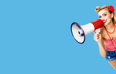Photo of happy excited woman holding mega phone and saying something. Blond girl in pin up style with megaphone, over blue color background with copy space area. Female model in retro vintage concept.