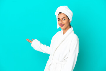 Young woman in a bathrobe over isolated blue background extending hands to the side for inviting to come