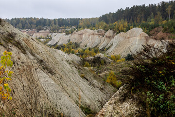 A landscape of a chalk quarry for the production of chalk and sand for use in the construction industry. A mixed forest of green and yellow autumn colors grows at the top of the quarry.