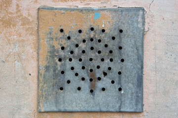 Old square metal ventilation grate with holes at building wall