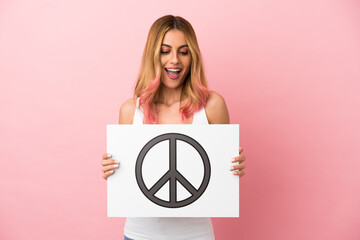 Young woman over isolated pink background holding a placard with peace symbol