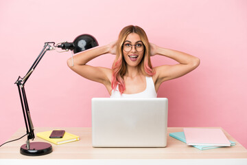 Young student woman in a workplace with a laptop over pink background laughing