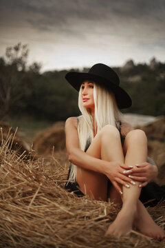 Beautiful woman cowboy in dress and hat posing next to a haystack. Fashion concept.