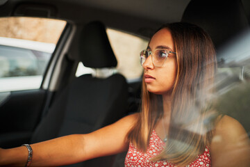 Young brunette spanish woman sitting on car checking rear mirror