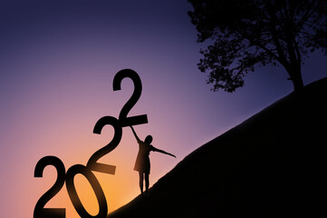 silhouettes of happy women lining up numbers In the concept of the beginning of the new year 2022. The hills, big trees, and the first light of the new day are the backgrounds. 