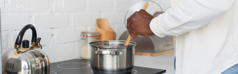 cropped view of young african american man cooking in kitchen, banner
