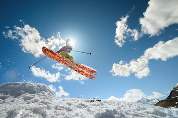 Fototapeta na wymiar A woman skier makes a jump trick, covering the sun. Flying skier against the background of the sky and clouds.