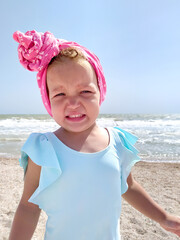 Capricious child on the beach. Portrait of a little girl being naughty.