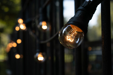 Light bulb chain outside at an iron fence at the summer