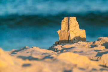 A small sand castle tower built on a beach with blue sea tide in the blurred background on early...