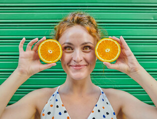 Young woman with orange hair playing with an fresh orange on green background