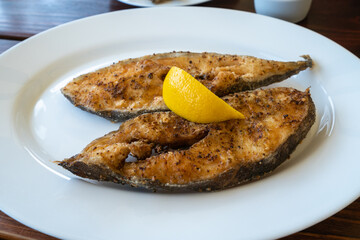 Closeup shot of freshly fried halibut fillets with lemon on a white plate in a local pub in Jastarnia, Poland. Polish local seafood of the Baltic coast.