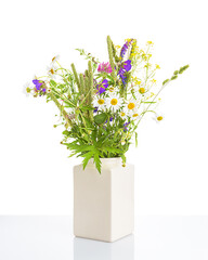 Bouquet of field flowers in a ceramic white vase on a white background, front view.