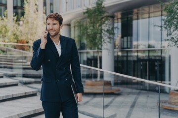 Fashionable unshaven businessman uses modern technologies has telephone conversation holds gadget