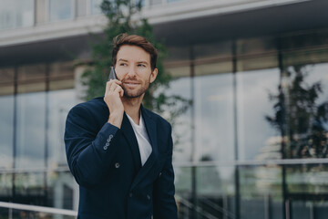 Male entrepreneur talks via phone solves urgent problems poses near business center