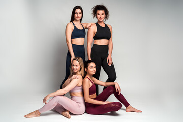 Fototapeta na wymiar Group of sportswomen with different appearance and type of figure posing together in sport outfit against a white background. Stock photo