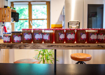 Freshly filled jars of marmelade standing in a kitchen.