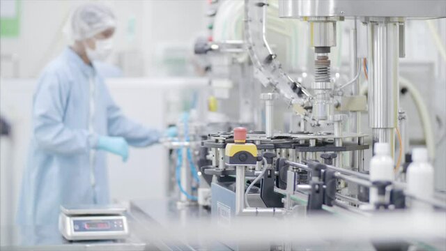 Factory worker operates bottling machinery on the production line. 