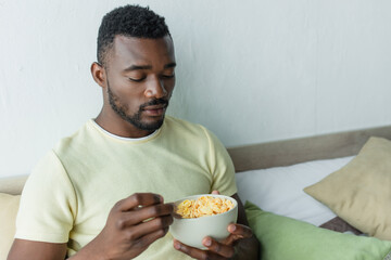 bearded african american man looking at corn flakes in bowl