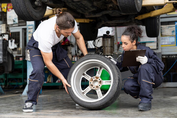 Male and female car mechanic worker checking, repair and maintenance wheel at auto repair shop. Group of  mechanic vehicle service maintenance examining wheel tire at garage. Auto car repair service
