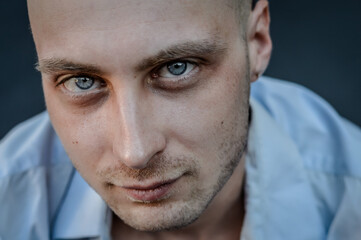 very close portrait of a young bald man with blue eyes and a blue shirt looking intently at the camera