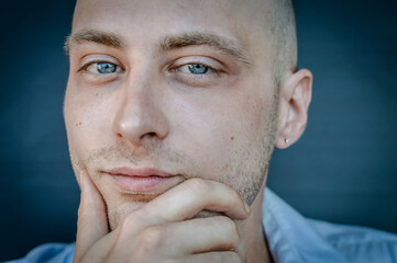 portrait of a young bald man holding his chin with his hand and looking thoughtful as he looks in front of him