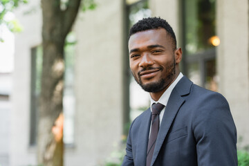 smiling african american businessman in suit looking at camera outside