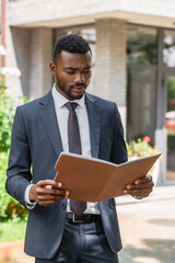 focused african american businessman holding folder outside