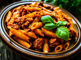 Penne with minced meat, tomato sauce, parmesan cheese, basil and vegetables served on wooden table