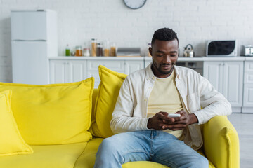 joyful young african american man texting on smartphone