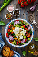 Fresh Greek salad - feta cheese, cherry tomatoes, cucumber, black olives and onion on wooden table
