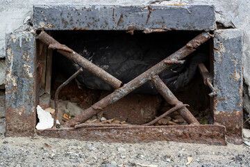 Rough rusty metal ventilation grate in the basement wall, plugged with a plastic bag