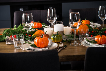 Autumn table setting with plate, glass, cutlery and autumn decor at wooden table. Thanksgiving food festive dinner concept.