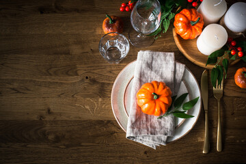 Autumn table setting with plate, pumpkin and candles at wooden table. Thanksgiving food festive dinner concept. Top view with copy space.