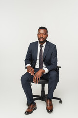 african american businessman in suit sitting in office chair isolated on grey