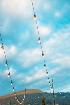 Light bulbs retro garland hanging in a restaurant or cafe in the garden at evening time. Lighting decor. Bright blue sky with clouds