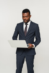 african american businessman in suit using laptop isolated on grey