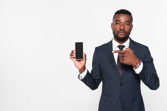 african american businessman in suit pointing at smartphone with blank screen isolated on grey