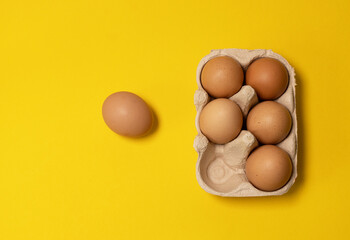 Easter brown chicken eggs in eco basket and one egg on yellow background. Fresh egg on morning breakfast, flat lay, copy space.