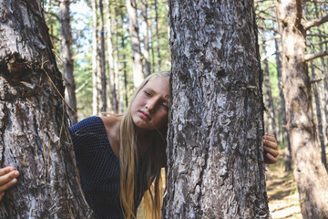 A sad blonde girl stands between the trees of the pines in the forest selective focus, nature protection.
