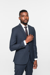 african american businessman in suit adjusting jacket isolated on grey