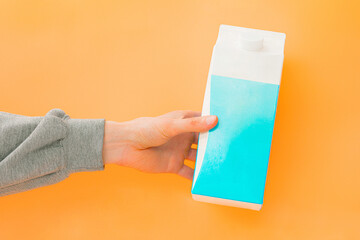 Man's arm holds a package of milk on orange background. Human. Male. Drink. Hand. Gray sleeve....