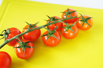 Bright red cherry tomatoes on white clean plastic cutting board with a kitchen knife