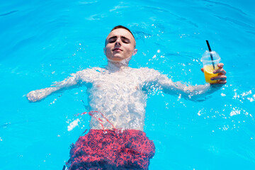 From above of carefree relaxed young handicapped male with amputated arm enjoying of cocktail and lying on blue water surface in outdoor swimming pool, while enjoying summertime