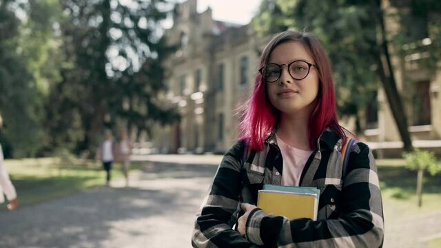 Serious hipster school girl adjusting eyeglasses, posing on camera with books