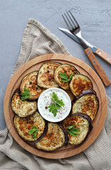 Fried eggplant on a wooden plate on a gray background. Vegetable appetizer of eggplant. Top view. Vertical photo.