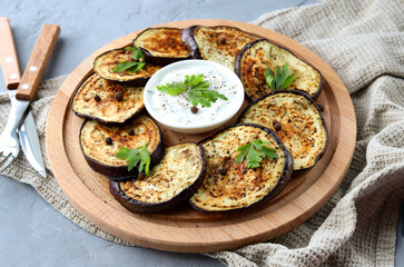 Grilled eggplant with spices, herbs and sauce on a wooden plate on a gray background. A healthy snack. Selective focus