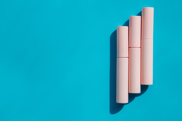 pink tubes of cosmetics on a blue background. Copy space. Closed tubes of lipstick, liquid lip gloss, mascara, eyeliner
