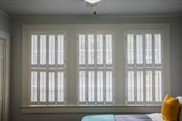Three large windows with cream colored plantation shutters that are closed on the interior of a...