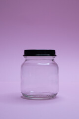 Small glass jar with metal lid on purple background
